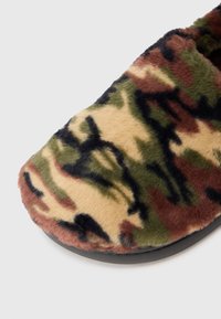 Chausson doux et moelleux avec un motif camouflage brun, vert, beige et noir, et une semelle noire sur fond blanc.