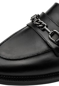 Mocassin en cuir noir avec un détail chaîne métal argenté à l'avant et des coutures visibles le long des bords.