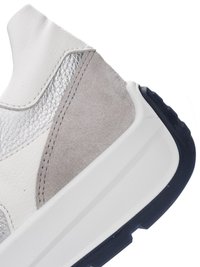 Close-up of a sneaker's heel showing white leather, silver textured panel, grey suede overlay, and thick white sole with black tread edge.