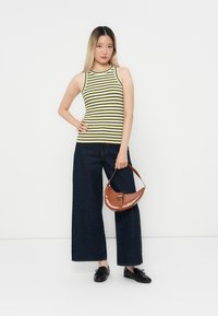 Grünes und weiß gestreiftes geripptes Tanktop, dunkle weit geschnittene Jeans, braune strukturierte Handtasche und schwarze Schuhe.
