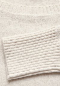 Maglione color crema chiaro con una finitura morbida e testurizzata. Presenta un colletto a coste e un motivo a righe sui polsini per un tocco in più.