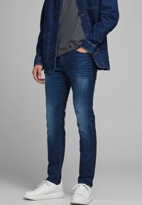 Mörkblå denimjeans med smal passform, med lätt blekning och kontrastsömmar. Matchade med en grå t-shirt och vita sneakers.
