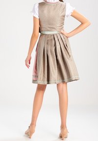 Femme portant une robe plissée beige à mi-longueur avec des garnitures vert pâle, un haut à manches bouffantes blanc et des escarpins nude, vue de dos.