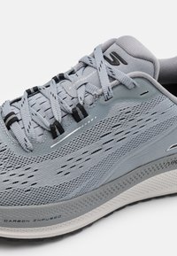 Baskets de sport grises avec une tige en maille respirante, des détails texturés et une semelle infusée de carbone pour un soutien et une durabilité accrus.