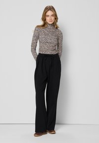 Leopardprint lange mouw top gecombineerd met hooglopende zwarte wijde broek en bruine schoenen. Gladde stof met een aansluitend ontwerp.