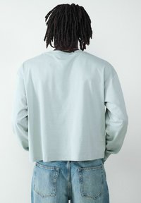 Jasnoniebieska koszula z długim rękawem o skróconym kroju i miękkiej teksturze. W połączeniu z jasnoniebieskimi dżinsami mającymi podwójne tylne kieszenie.
