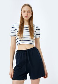 Top corto bianco a coste con righe orizzontali blu navy, abbinato a pantaloni corti casual blu navy con vita elasticizzata e coulisse.