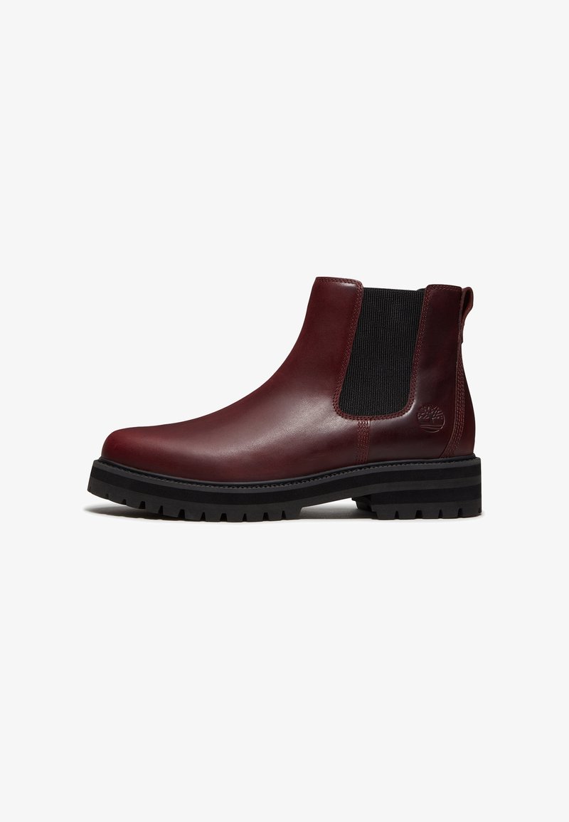 Bottine Chelsea en cuir rouge foncé avec panneau latéral élastique noir, semelle épaisse à crampons noire, logo embossé sur le côté et languette à l’arrière.