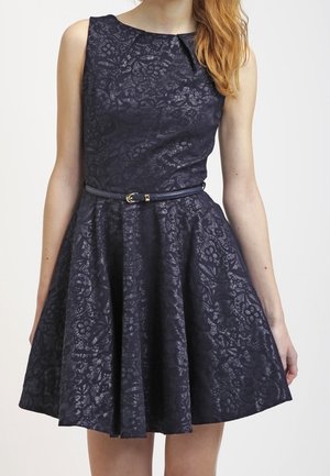 Abito senza maniche in pizzo floreale blu navy scuro con corpetto aderente, gonna svasata e sottile cintura nera in vita.