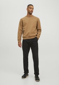 Brauner Sweatshirt aus weichem Stoff mit Rundhalsausschnitt, kombiniert mit schwarzen Hosen und schwarzen Schnürstiefeln mit leichter Sohle. Minimalistisches Design.