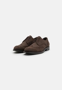 Brune semskede pensko med spiss tå, mønstrede brogue-detaljer og en tynn, flat hæl. Snøringene har klassiske snorløft.