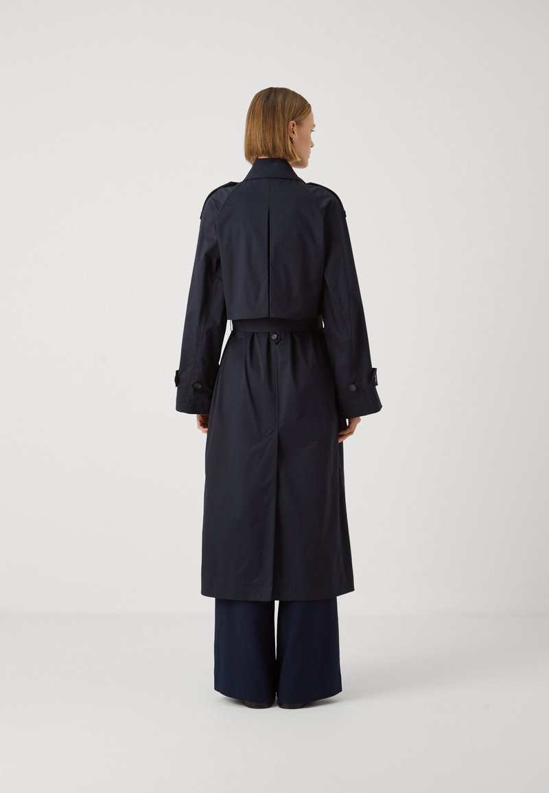 Cappotto trench navy con vita cintata, maniche lunghe e design doppiopetto. Presenta epaulette sulle spalle e uno spacco sul retro.