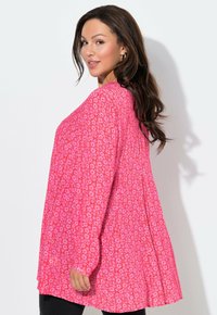 Jasně růžová halenka s květinovým vzorem, dlouhými rukávy, volným střihem a kulatým výstřihem. Látka má měkkou texturu.