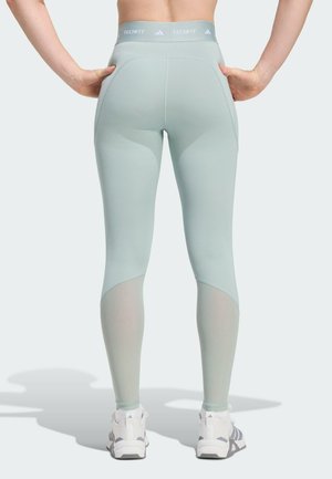 Svijetlozelene kompresijske tajice s visokim strukom, mrežastim detaljima na listovima i glatkim, rastezljivim materijalom.