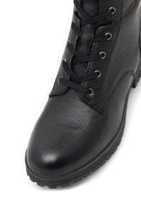 Stivale alla caviglia in pelle nera con punta rotonda, superficie texturizzata, occhielli in metallo e lacci neri. Suola in gomma con motivi antiscivolo.