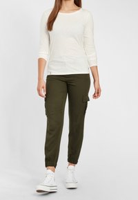 Hellbeige Langarmshirt kombiniert mit olivgrünen Cargo-Hosen mit Seitentaschen und elastischen Bündchen, getragen mit weißen Sneakern im High-Top-Stil.