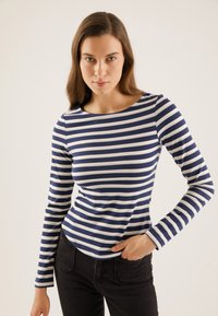 Long-sleeve top featuring navy and white horizontal stripes, crew neckline, fitted design, and soft cotton material. Black pants visible.