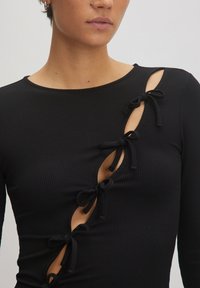 Schwarzes, geripptes Longsleeve-Top mit Cut-Out-Details und Stoffbändern an der Seite, die ein asymmetrisches Design schaffen.