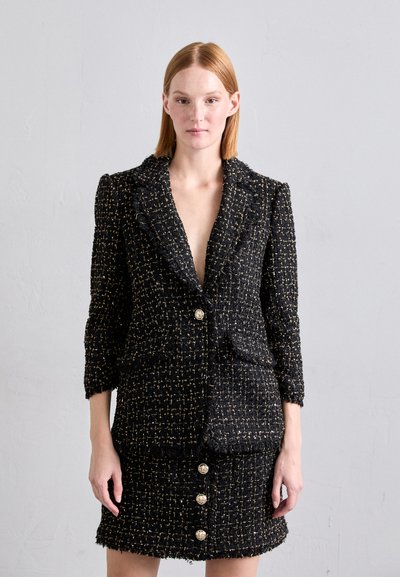 Completo giacca e gonna in tweed nero e oro con una finitura strutturata, rever a punta, chiusura con singolo bottone e dettagli con bottoni dorati.