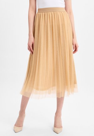 Plissierter Midirock aus hellbeige Tüll mit breitem Taillenbund. Verfügt über mehrlagigen Stoff für Textur und Bewegung, kombiniert mit neutralen Absätzen.