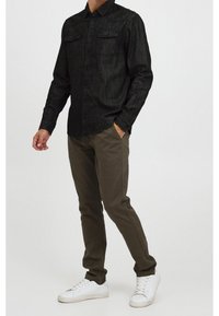 Musta denim-painikepaita, jossa on kaksi rintataskua, yhdistettynä oliivinvihreisiin slim-fit-housuihin ja valkoisiin tennareihin.