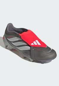 Szürke focicipő texturált hálós felsőrésszel, piros zokniszerű szegéllyel, fehér háromcsíkos logóval és szegecses gumi talppal a tapadás érdekében.