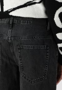 Zwarte denim jeans met een klassiek vijf-pocket ontwerp, voorzien van zichtbare stiksels en een merkpatch van zwart leer op de achterkant van de tailleband.