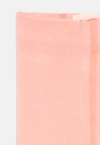 Calzini rosa chiaro con una texture liscia, caratterizzati da un bordo a costine e una cucitura che corre lungo un lato.