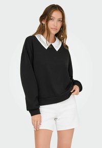 Felpa nera con colletto bianco ricamato, maniche lunghe e fondo a costine, abbinata a pantaloni corti bianchi. Design semplice e moderno.