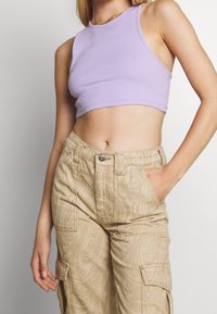Haut court côtelé violet clair avec un col montant, associé à un pantalon cargo beige texturé avec poches latérales et coupe décontractée.