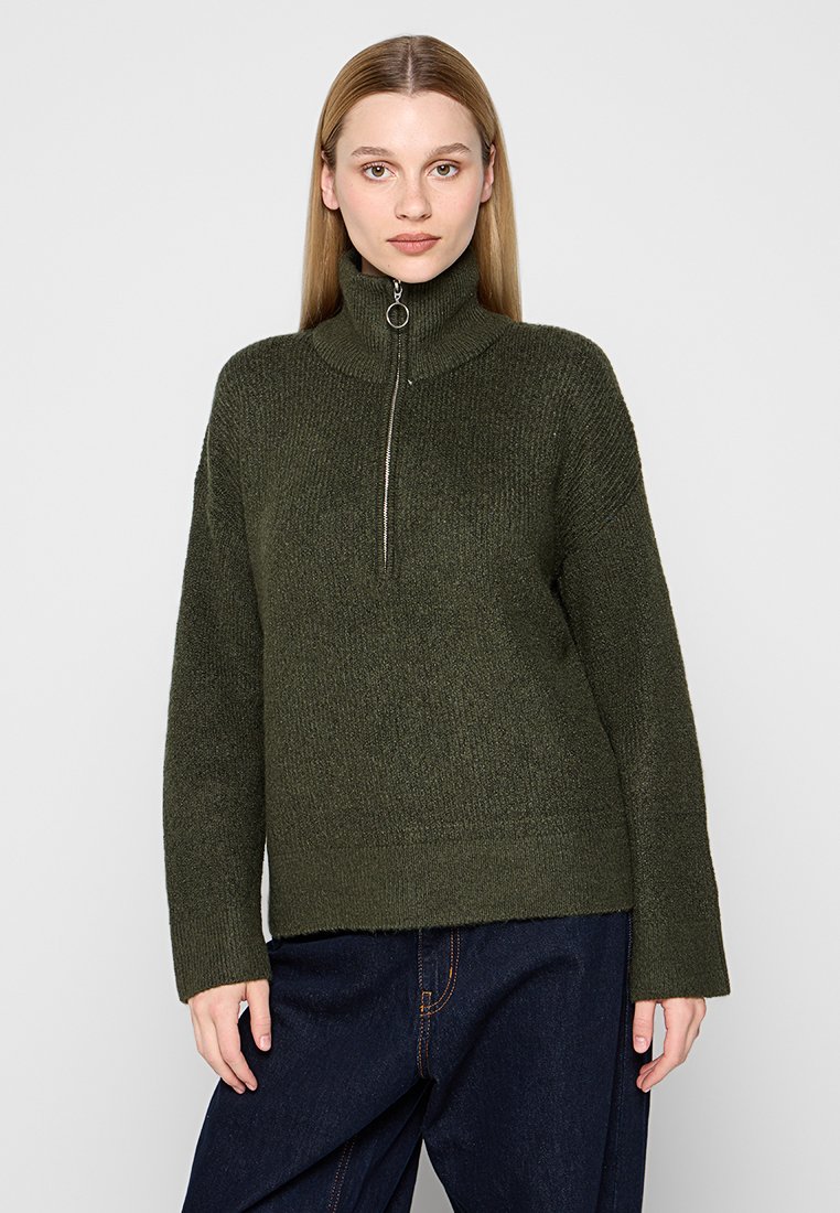Dunkelgrüner, gestrickter Pullover mit einem hohen Kragen und einem halben Reißverschluss. Lockere Passform mit langen Ärmeln und gerippter Struktur. Keine auffälligen Muster.