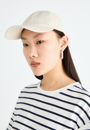 Căciulă bej din in cu bor lactic, asortată cu o cămașă albă cu dungi orizontale bleumarin. Designul este simplu și modern.