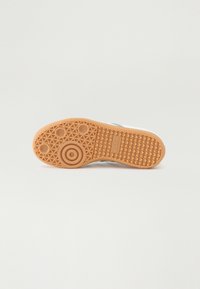 Sola de sapato com um design em borracha texturizada castanha, apresentando padrões circulares e triangulares, com um logótipo em relevo. Fundo branco limpo.