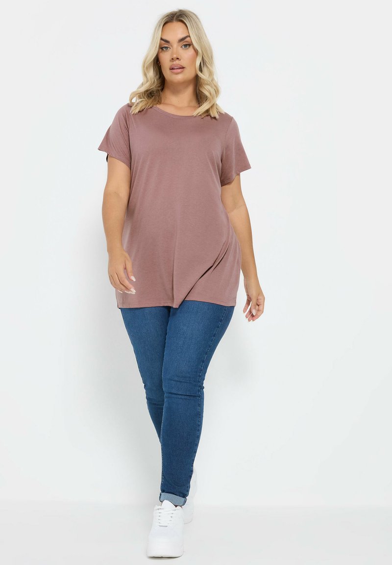 Petal pink t-shirt med korte ærmer, afslappet pasform og buet kant, parret med mørkeblå skinny jeans og hvide sneakers.
