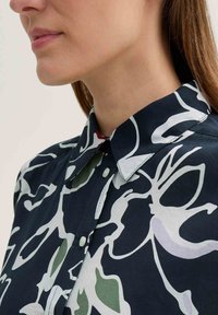 Floral-patterned shirt in dark navy, featuring white and pale green designs, with a classic collar and button closure at the neck.