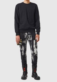 Felpa nera con tasche frontali, abbinata a pantaloni cargo neri e bianchi con motivo a fantasia. Stivali da combattimento neri con dettagli rossi.