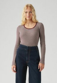 Lange mouw top in crèmekleurige en bordeaux horizontale strepen, met een geschulpte halslijn. Gecombineerd met high-waisted donkerblauwe jeans.