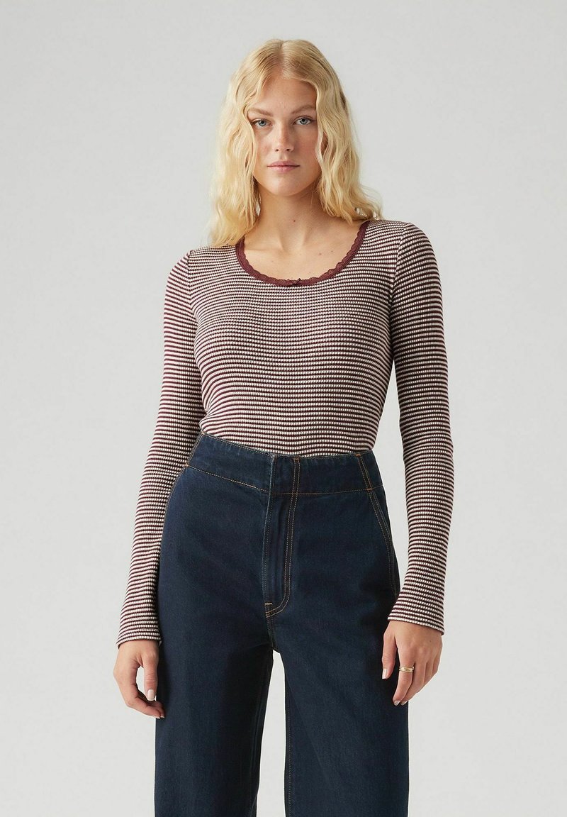 Lange mouw top in crèmekleurige en bordeaux horizontale strepen, met een geschulpte halslijn. Gecombineerd met high-waisted donkerblauwe jeans.