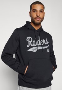 Juodas džemperis, pagamintas iš medvilnės mišinio, su pilku išsiuvinėtų "Raiders" tekstu ir logotipu, kengūros tipo kišene ir virvute. 