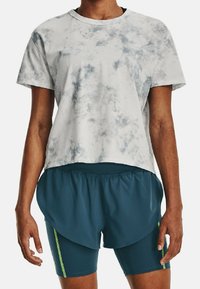 Camiseta cortada de color gris claro con un patrón de tie-dye azul, combinada con pantalones cortos de color verde azulado oscuro con un diseño en capas y acentos en verde neón.