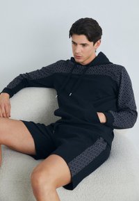 Black hoodie with patterned gray accents on sleeves and torso, paired with black shorts featuring matching side panels. Soft texture.