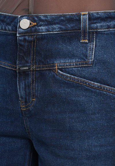 Donkerblauwe denim jeans met oranje stiksels, een zilveren knoopsluiting en een "CLOSED" etiket bij de tailleband. Regular fit, minimale slijtage.