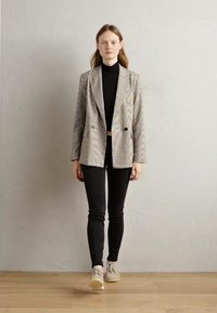 Patterned grey blazer with peak lapels, double-breasted design; paired with a black turtleneck and slim black pants, finished with beige shoes.