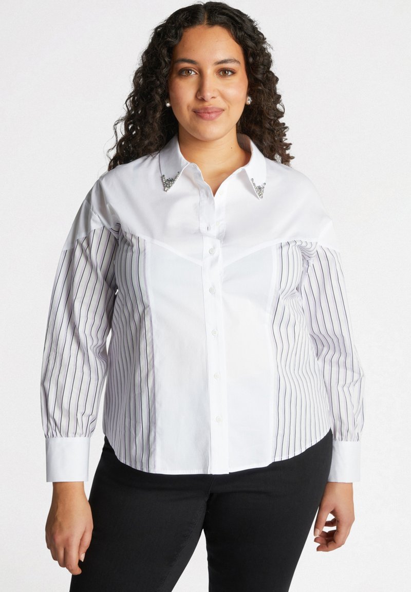 Chemise blanche avec des manches rayées, col orné, devant à boutons et légère draperie. Elle est fabriquée en coton doux et a une coupe structurée.