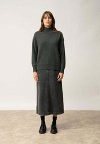 Ciemnoszary dzianinowy sweter z wysokim kołnierzem, zestawiony z długą dżinsową spódnicą w ciemnym odcieniu. Model nosi czarne buty i skarpetki. Gładka tekstura.