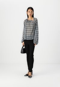 Top leggero e trasparente a quadri grigio e nero, con maniche lunghe a sbuffo e scollatura arricciata. Abbinato a pantaloni neri aderenti e tacchi.