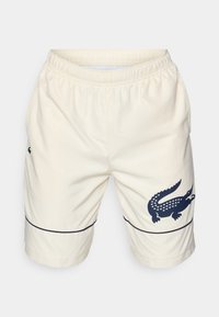 Cream-colored shorts made of textured material with an elastic waistband. Features a navy crocodile logo and a blue line detail at the hem.