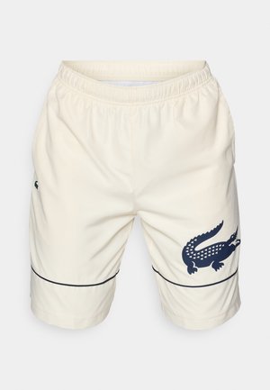 Shorts couleur crème en matière texturée avec une taille élastique. Présente un logo crocodile marine et un détail de ligne bleue au niveau de l'ourlet.