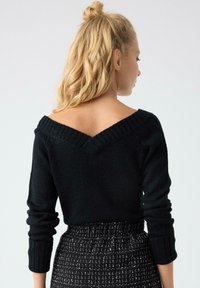 Suéter negro de punto con escote en V y puños acanalados, que presenta una textura suave. Combinado con una falda de cintura alta en blanco y negro con textura.