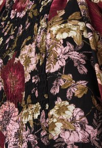 Tessuto floreale caratterizzato da grandi fiori rosa e bordeaux su uno sfondo nero, con una texture arricciata e un pannello laterale nero in contrasto.